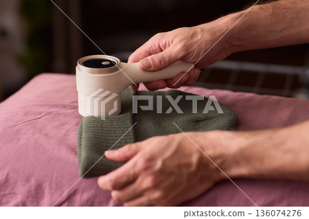Close view of lint tool on wool, Man using lint roller to clean wool hat texture, Detailed scene of hand grooming fuzz from soft knitted wool hat with lint roller 136074276
