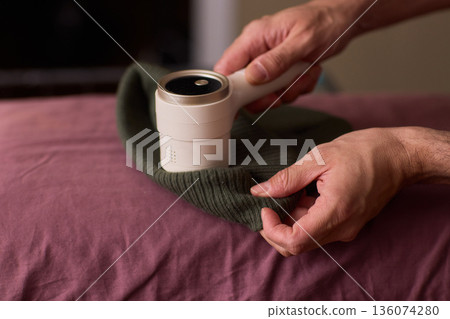 Close view of lint tool on wool, Man using lint roller to clean wool hat texture, Detailed scene of hand grooming fuzz from soft knitted wool hat with lint roller 136074280