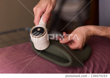 Close view of lint tool on wool, Man using lint roller to clean wool hat texture, Detailed scene of hand grooming fuzz from soft knitted wool hat with lint roller Close view of lint tool on wool, Man using lint roller to clean wool hat texture, Detailed scene of hand grooming fuzz from soft knitted wool hat with lint roller 136074283