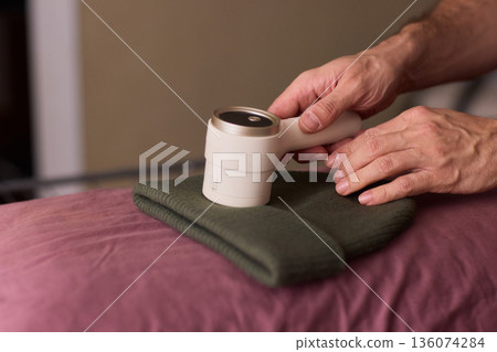 Close view of lint tool on wool, Man using lint roller to clean wool hat texture, Detailed scene of hand grooming fuzz from soft knitted wool hat with lint roller 136074284