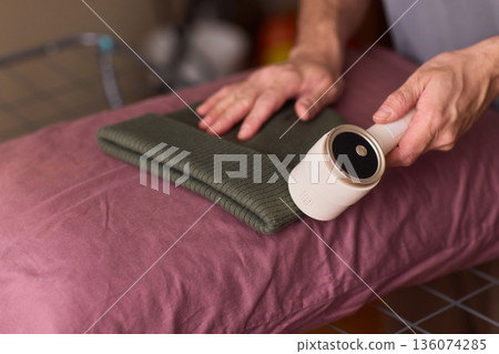 Close view of lint tool on wool, Man using lint roller to clean wool hat texture, Detailed scene of hand grooming fuzz from soft knitted wool hat with lint roller Close view of lint tool on wool, Man using lint roller to clean wool hat texture, Detailed scene of hand grooming fuzz from soft knitted wool hat with lint roller 136074285