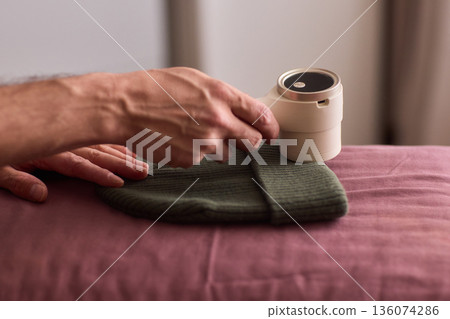 Close view of lint tool on wool, Man using lint roller to clean wool hat texture, Detailed scene of hand grooming fuzz from soft knitted wool hat with lint roller Close view of lint tool on wool, Man using lint roller to clean wool hat texture, Detailed scene of hand grooming fuzz from soft knitted wool hat with lint roller 136074286