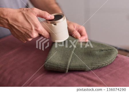 Close view of lint tool on wool, Man using lint roller to clean wool hat texture, Detailed scene of hand grooming fuzz from soft knitted wool hat with lint roller 136074290