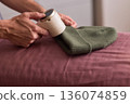 Close view of lint tool on wool, Man using lint roller to clean wool hat texture, Detailed scene of hand grooming fuzz from soft knitted wool hat with lint roller 136074859