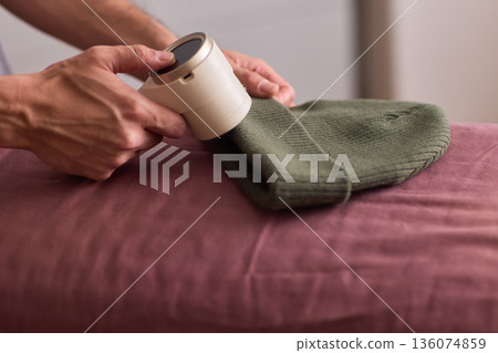 Close view of lint tool on wool, Man using lint roller to clean wool hat texture, Detailed scene of hand grooming fuzz from soft knitted wool hat with lint roller 136074859