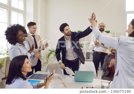Two men giving high five celebrating business achievement on workplace in office. 136075190