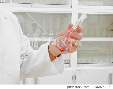 Laboratory Researcher Holding Round Flask And Dropper, CloseUp Of Precise Transfer Of Colored Liquid, White Laboratory Researcher Holding Round Flask And Dropper, CloseUp Of Precise Transfer Of Colored Liquid, White 136075296