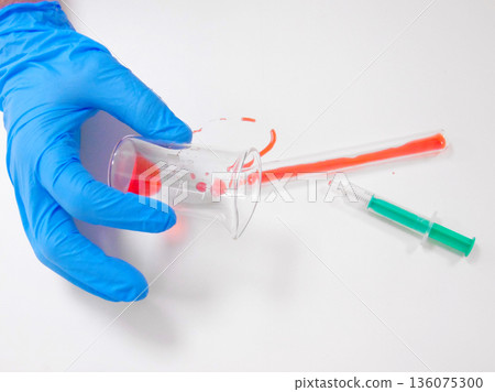Gloved Hand Holding Beaker While Pouring Red Reagent Over White Surface, Experimental Mixing And Spill Risk 136075300