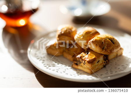 Scones and tea set on white plates illuminated by natural light from a window Scones and tea set on white plates illuminated by natural light from a window 136075410