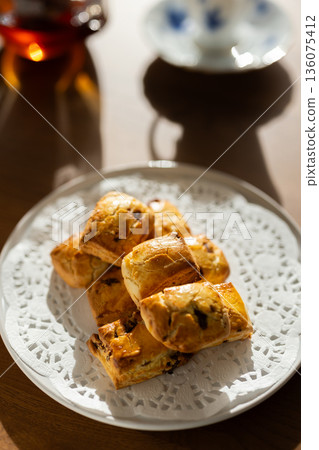 Scones and tea set on white plates illuminated by natural light from a window Scones and tea set on white plates illuminated by natural light from a window 136075412