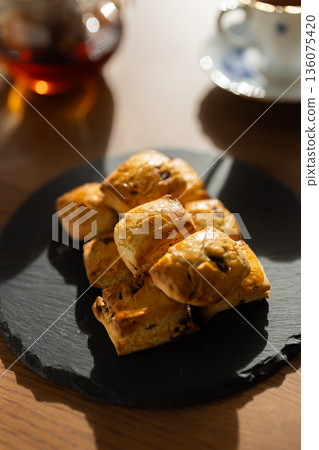 Scones and tea set on a black plate illuminated by natural light from the window Scones and tea set on a black plate illuminated by natural light from the window 136075420