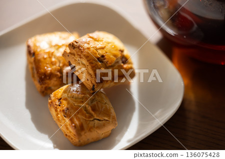 Scones and tea set on white plates illuminated by natural light from a window Scones and tea set on white plates illuminated by natural light from a window 136075428