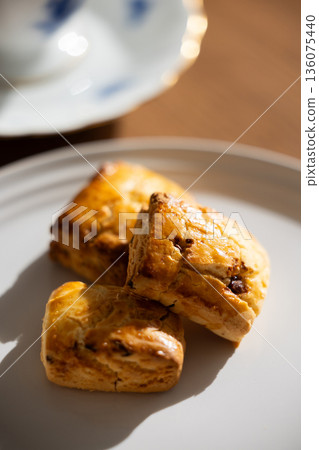 Scones and tea set on white plates illuminated by natural light from a window Scones and tea set on white plates illuminated by natural light from a window 136075440