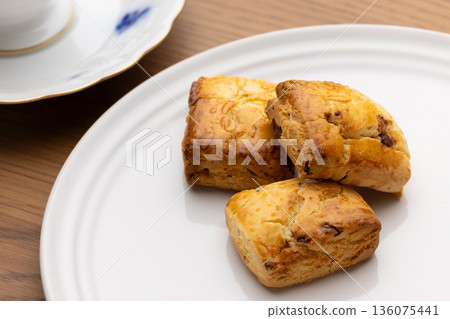 Scones and tea set on white plates illuminated by natural light from a window Scones and tea set on white plates illuminated by natural light from a window 136075441
