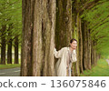 A smiling woman strolling along the Metasequoia tree-lined path in fresh greenery 136075846