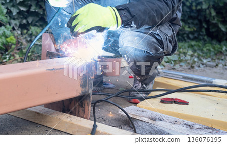 Construction worker in protective mask and gloves welding a steel beam outdoor Construction worker in protective mask and gloves welding a steel beam outdoor 136076195