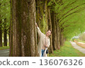 A smiling woman strolling along the Metasequoia tree-lined path in fresh greenery 136076326
