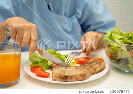 Asian elderly woman patient eating pork chop stake and vegetable salad for healthy food in hospital. Asian elderly woman patient eating pork chop stake and vegetable salad for healthy food in hospital. 136076771
