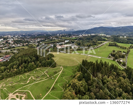 Rolling Hills With Woodland Paths, Elevated Grassy Fields With Winding Trails And Distant Town Views 136077274