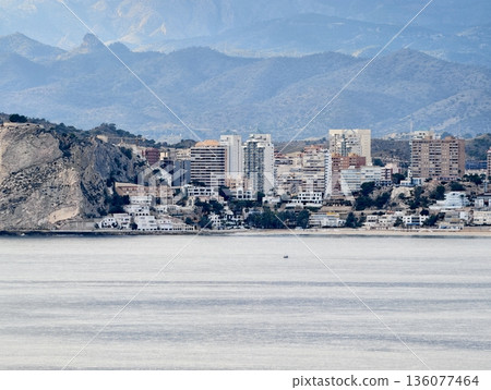 Coastal mountain scene, Distant peaks meet rugged shoreline, Hilly coast with towers and layered structures 136077464