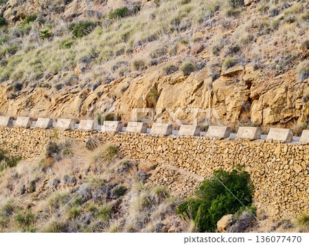 Weathered stones form hillside boundary, Rugged stone wall contours along dry slope landscape Weathered stones form hillside boundary, Rugged stone wall contours along dry slope landscape 136077470