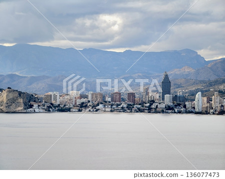 Urban horizon reflected over calm waters, City silhouette with mountain layers and tranquil bay Urban horizon reflected over calm waters, City silhouette with mountain layers and tranquil bay 136077473