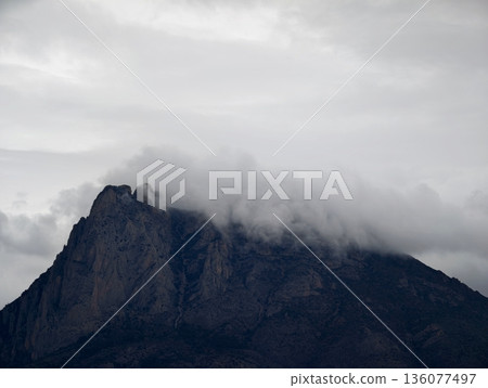 Secluded granite summit cloaked in brooding clouds amidst jagged cliffs and rugged terrain 136077497