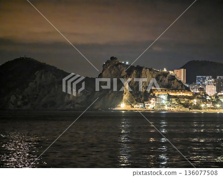 Peaceful coastal skyline at night, Quiet seaside fortress with glowing city lights and gentle waves Peaceful coastal skyline at night, Quiet seaside fortress with glowing city lights and gentle waves 136077508