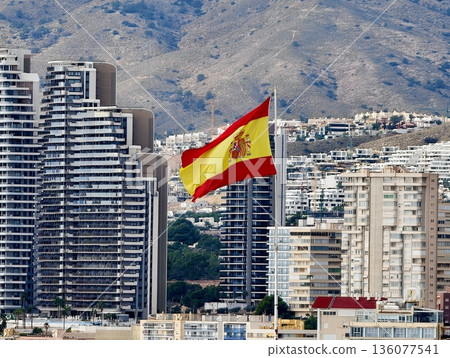 Spanish flag waving, Vibrant seaside cityscape with highrise buildings and sunny Mediterranean backdrop Spanish flag waving, Vibrant seaside cityscape with highrise buildings and sunny Mediterranean backdrop 136077541