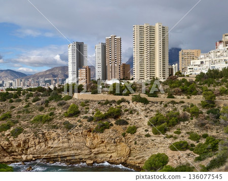 Urban towers situated along rocky coastlines with lush greenery and tranquil seaside environment 136077545
