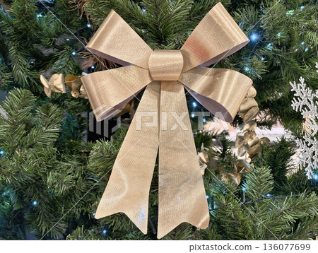 Decorative golden bow on green pine, Shimmering metallic ribbon adorns lush pine branches beautifully Decorative golden bow on green pine, Shimmering metallic ribbon adorns lush pine branches beautifully 136077699