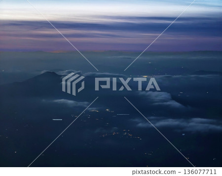 Serene dusk envelopes highland ridges with smoky cloud formations and distant illumination 136077711