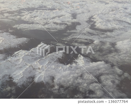 Cloudcovered mountain peaks in silence, Serene scene of snowy mountains veiled by clouds and mist Cloudcovered mountain peaks in silence, Serene scene of snowy mountains veiled by clouds and mist 136077764