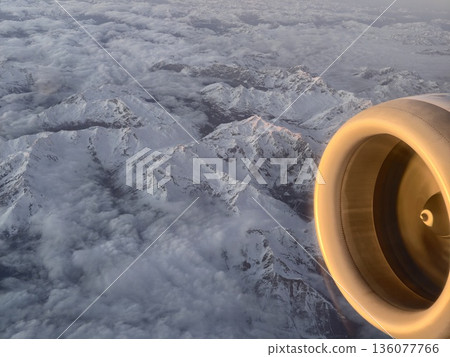 Engine whispers above icy mountain ranges, Jet engine shines with golden light over cold peaks 136077766