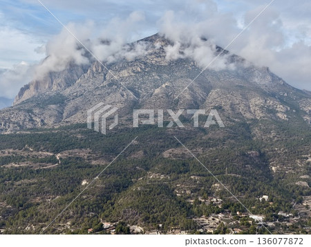 Gloomy peak above wooded hillside, Stormy summit rising over treecovered slopes and scattered houses 136077872