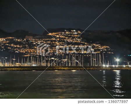 Serene night scene featuring sailboats against luminous shoreline reflections and tranquil water Serene night scene featuring sailboats against luminous shoreline reflections and tranquil water 136077897