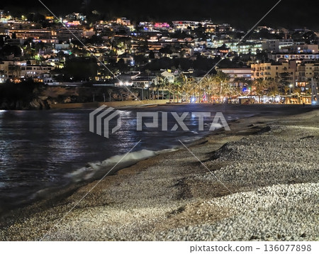 Sunset casts calm reflections on water, Serene night by ocean with city views glowing softly 136077898