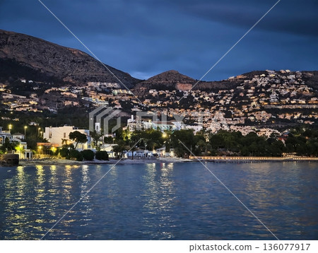 Silent ocean waters mirror coastal lights with gentle ripples in nighttime long exposure shots 136077917