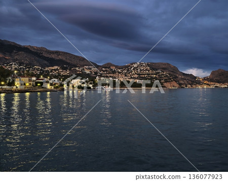 Serene and undisturbed sea reflects faint glow of distant city lights over gentle rolling hills Serene and undisturbed sea reflects faint glow of distant city lights over gentle rolling hills 136077923