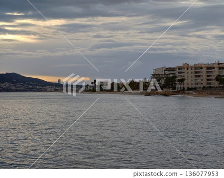 Tranquil dusk waterfront scenery, Quiet harbor scene with gentle waves and distant cityscape Tranquil dusk waterfront scenery, Quiet harbor scene with gentle waves and distant cityscape 136077953