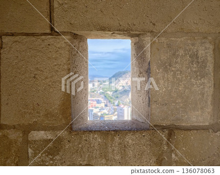 Coastal scene with masonry details, Sunlit coastal town framed by rustic stone window and masonry Coastal scene with masonry details, Sunlit coastal town framed by rustic stone window and masonry 136078063
