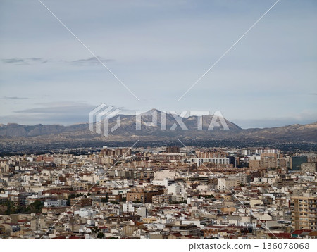 City rooftops and diverse architecture fade into distant mountain range under overcast sky 136078068