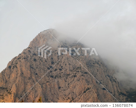 Granite peak under cloudy sky, Moody rocky summit displaying warm hues and textured surface Granite peak under cloudy sky, Moody rocky summit displaying warm hues and textured surface 136078074