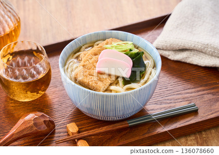 Kitsune udon noodles served with large fried tofu and kamaboko fish cake 136078660