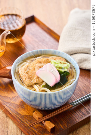 Kitsune udon noodles served with large fried tofu and kamaboko fish cake 136078673