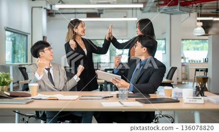 Businesswoman doing high five and man coworkers holding tablet making fist at wooden table in office Businesswoman doing high five and man coworkers holding tablet making fist at wooden table in office 136078820
