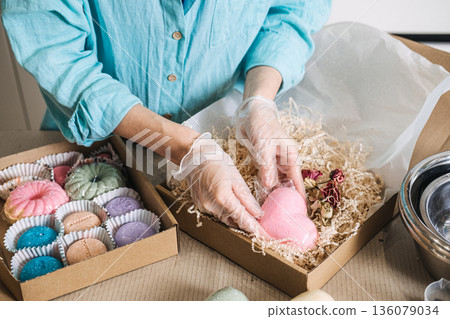 hands pour botanical mixture into metal bowl on digital scale surrounded by gift boxes. Neuro-Atmospheric Bathing, cortisol rescue, terpene bath, stress relief. 136079034