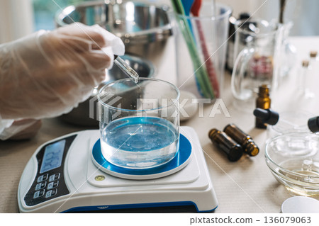 Gloved hand uses glass dropper to add liquid to beaker filled with clear fluid on digital scale. vegan PDRN, plant nucleotides, DNA repair, elasticity boost. Gloved hand uses glass dropper to add liquid to beaker filled with clear fluid on digital scale. vegan PDRN, plant nucleotides, DNA repair, elasticity boost. 136079063