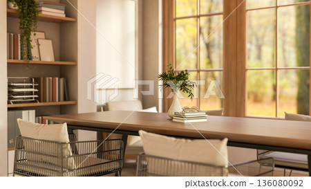 Books and vase on wooden table and metal armchairs with pillow cushion aside bookshelf and windows. Books and vase on wooden table and metal armchairs with pillow cushion aside bookshelf and windows. 136080092