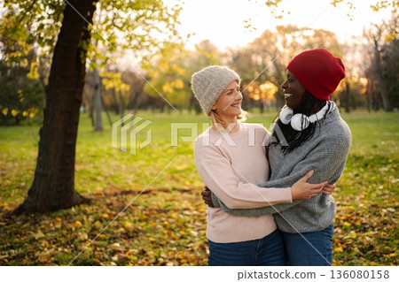 Diverse women embracing while enjoying autumn park outdoors Diverse women embracing while enjoying autumn park outdoors 136080158